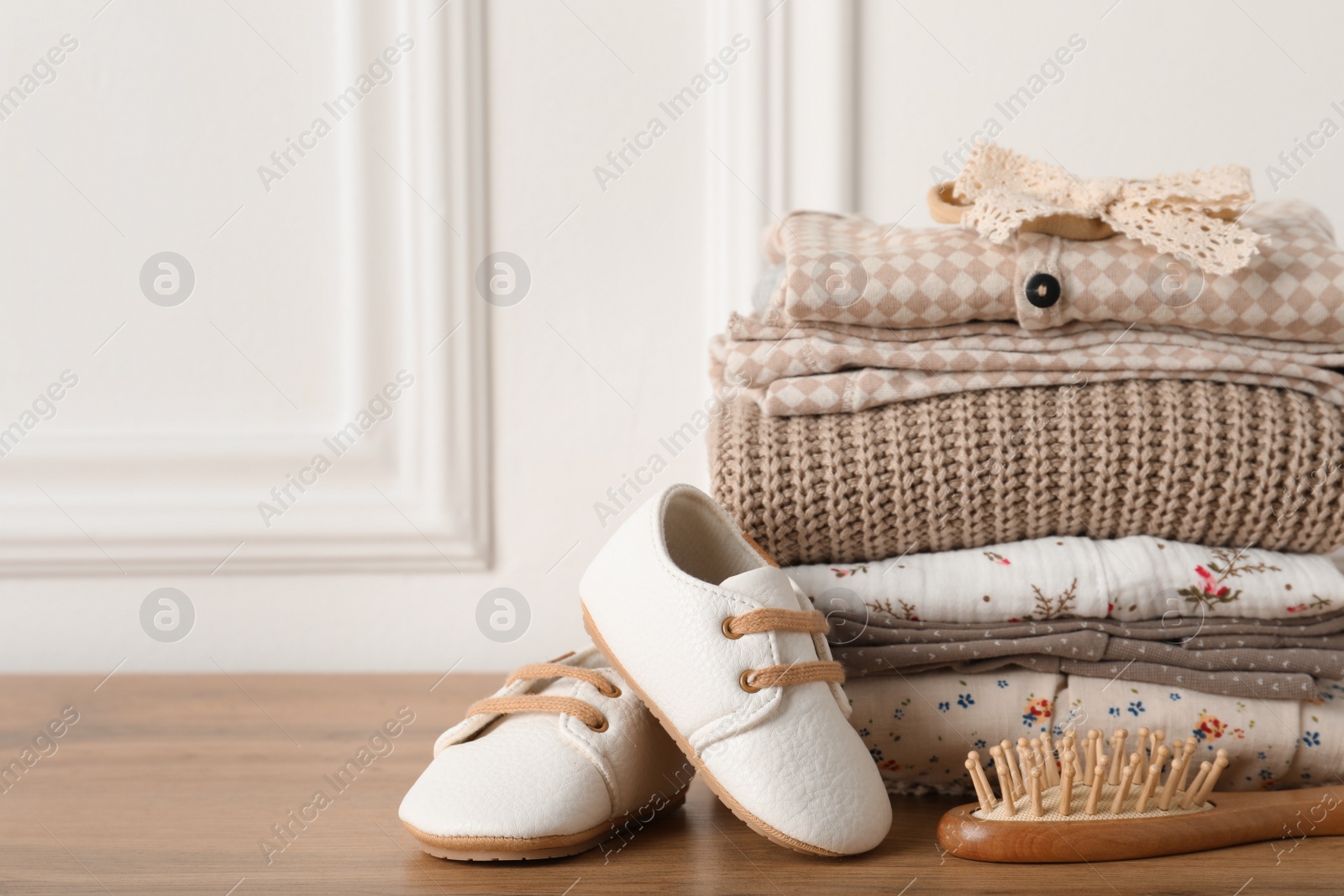 Photo of Baby clothes, shoes and hairbrush on wooden table