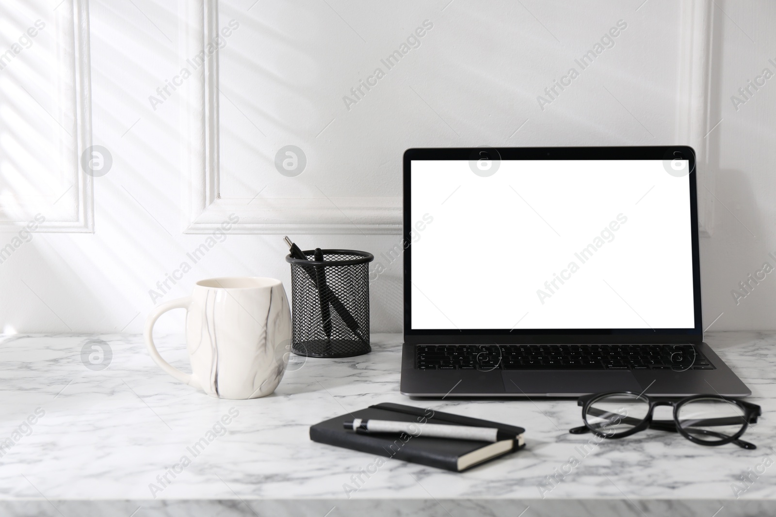 Photo of Office workplace with computer, glasses, cup and stationery on marble table near white wall