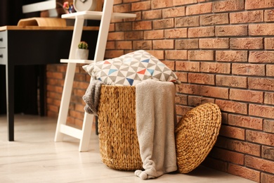 Photo of Wicker basket with blankets and pillow near brick wall, space for text. Idea for interior design