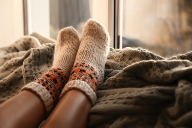 Woman in knitted socks relaxing on plaid near window at home, closeup