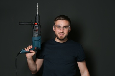 Photo of Young working man with rotary hammer on dark background