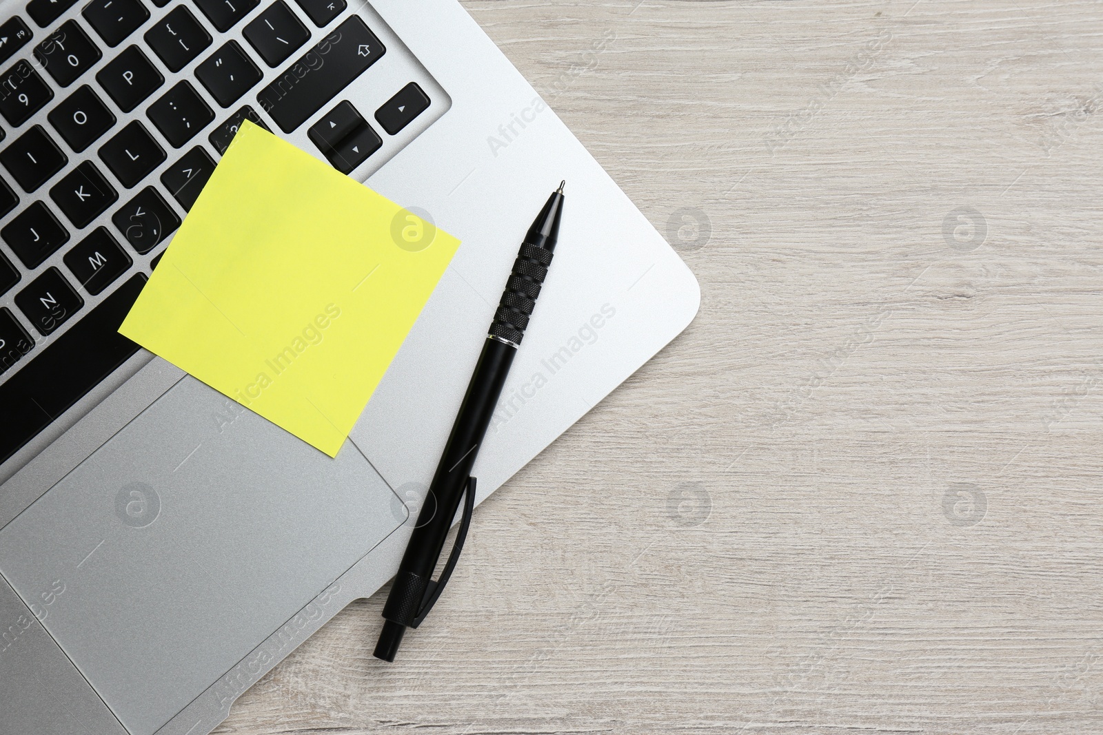 Photo of Laptop with blank sticky note and pen on white wooden table, top view. Space for text