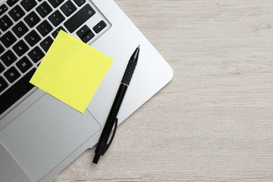 Laptop with blank sticky note and pen on white wooden table, top view. Space for text