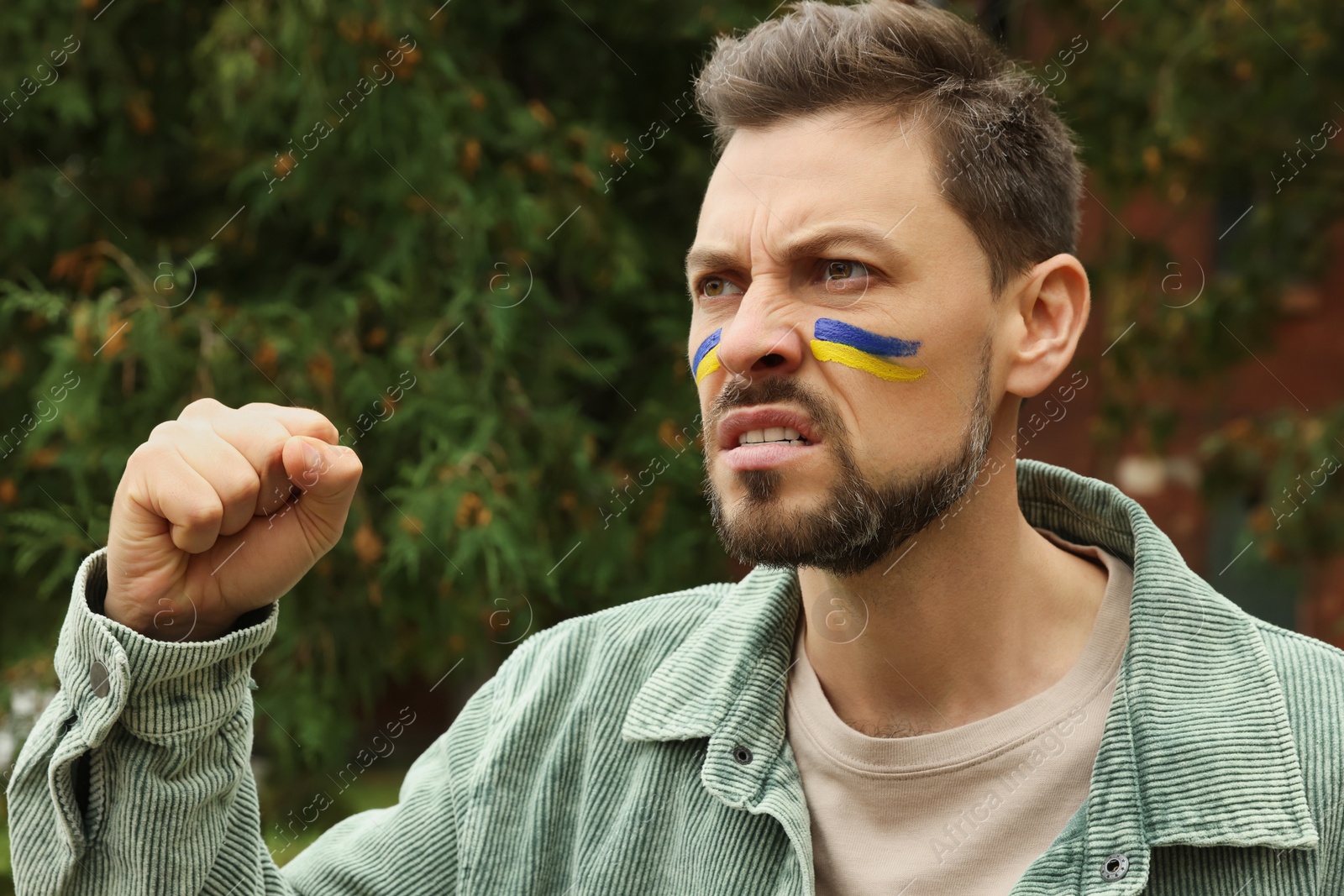 Photo of Angry man with drawings of Ukrainian flag on face outdoors