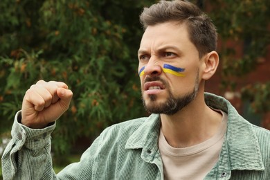 Photo of Angry man with drawingsUkrainian flag on face outdoors