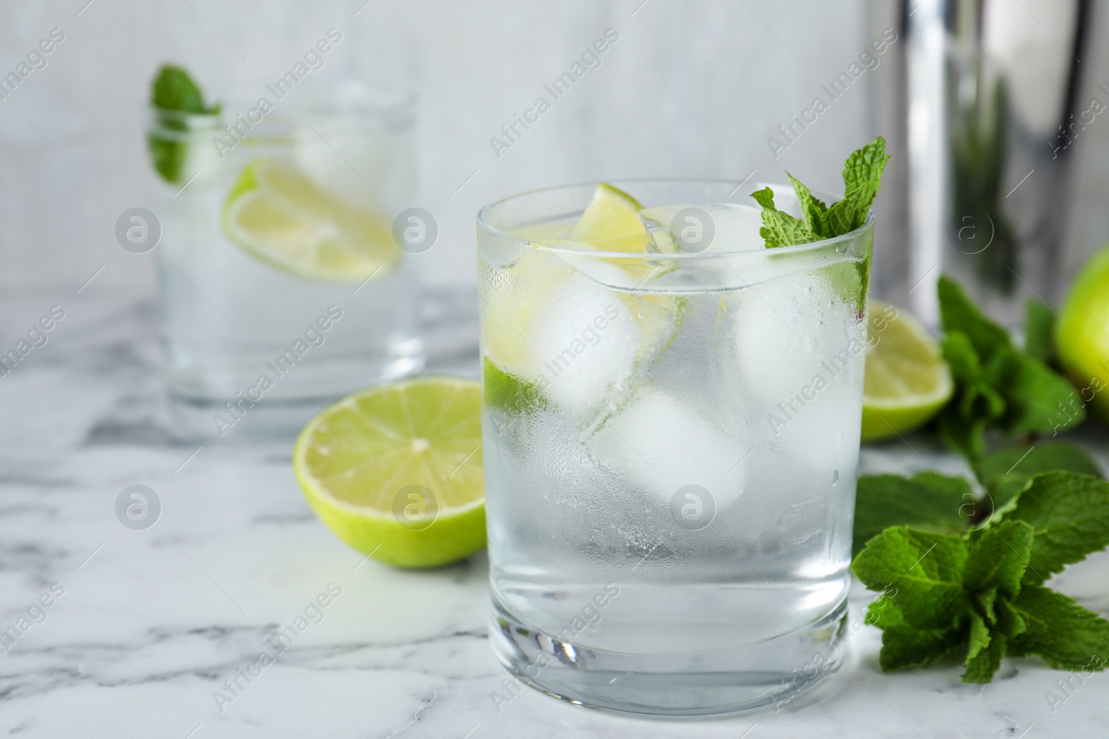 Photo of Glass of cocktail with vodka, ice and lime on white marble table