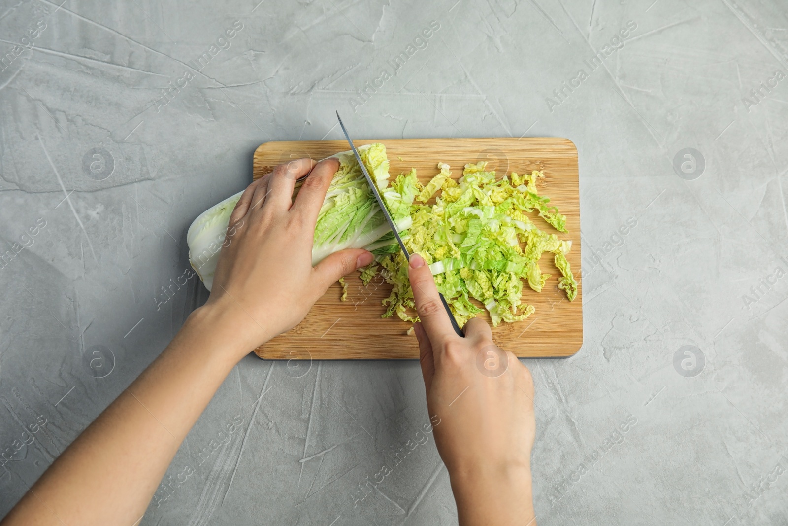 Photo of Woman cutting cabbage on wooden board, top view