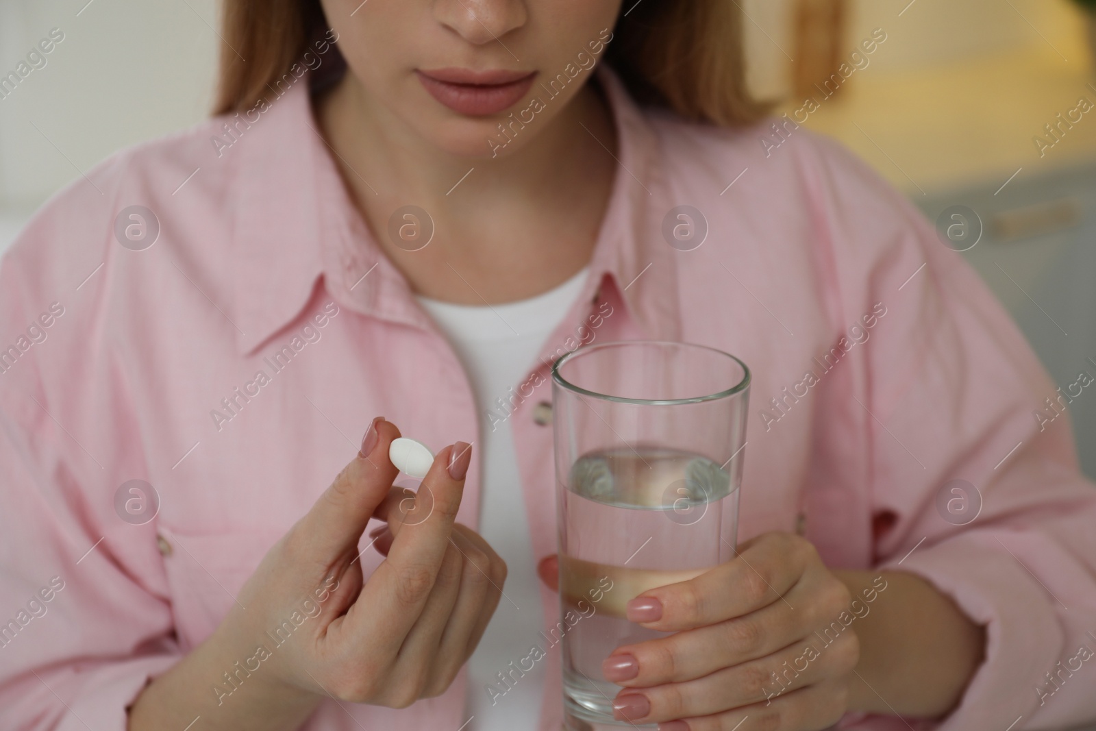 Photo of Young woman with abortion pill and water on blurred background, closeup