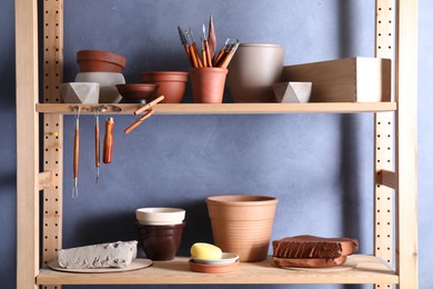 Photo of Set of different crafting tools and clay dishes on wooden rack in workshop