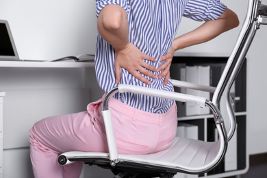 Woman with lower back pain sitting in office chair at table, closeup