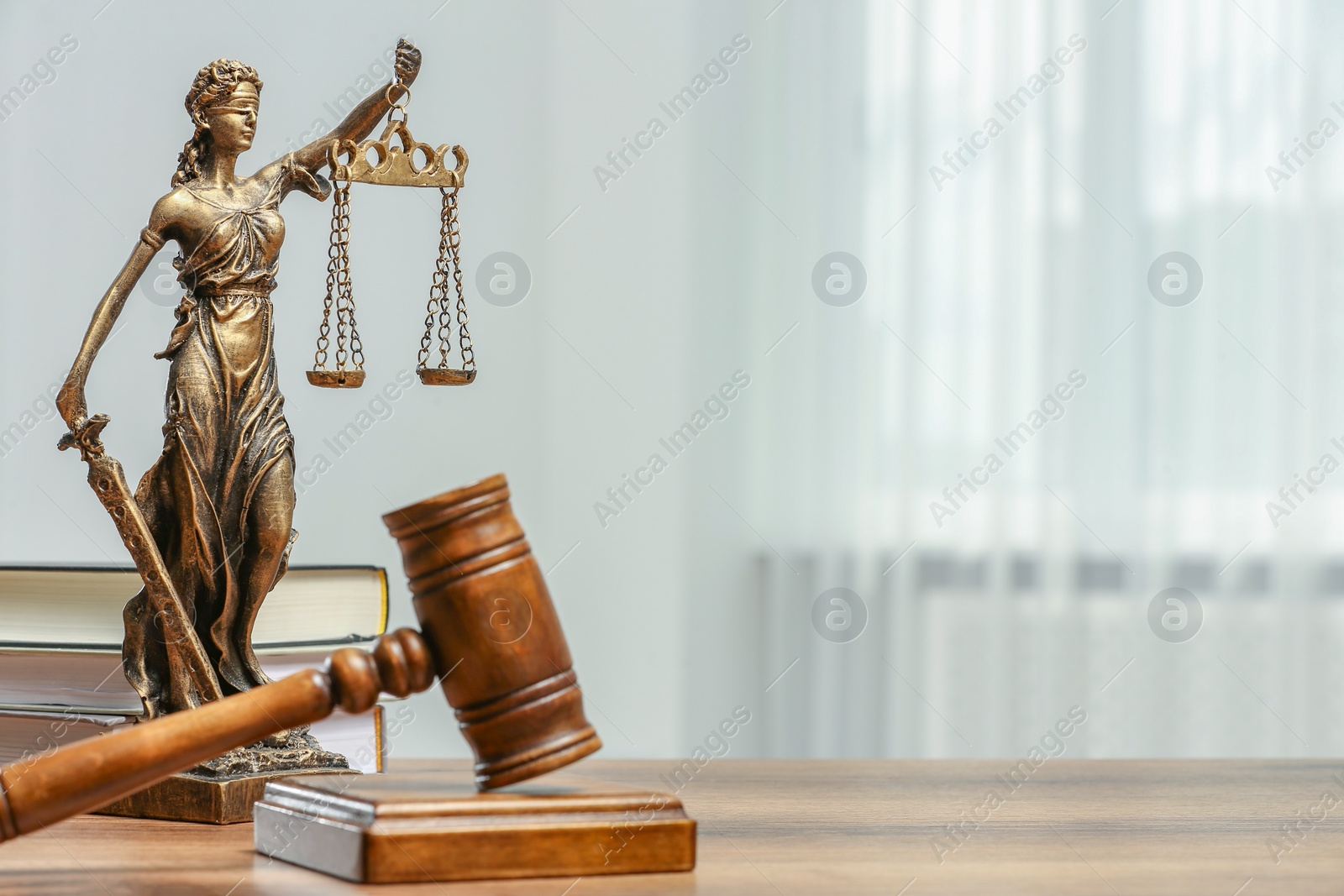 Photo of Figure of Lady Justice, gavel and books on table indoors, space for text. Symbol of fair treatment under law