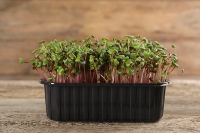 Photo of Fresh radish microgreens in plastic container on wooden table