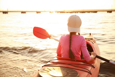 Photo of Little girl kayaking on river, back view. Summer camp activity