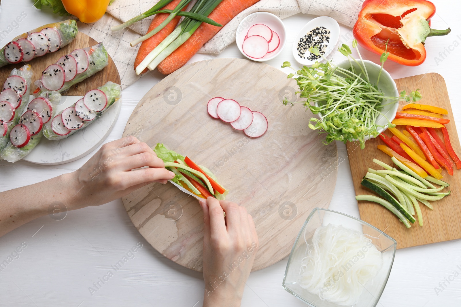 Photo of Woman wrapping spring roll at white wooden table with products, top view