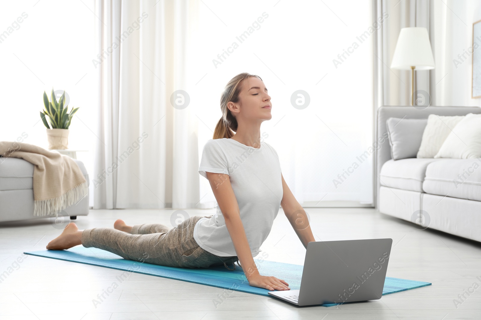 Photo of Woman having online video class via laptop at home. Distance yoga course during coronavirus pandemic