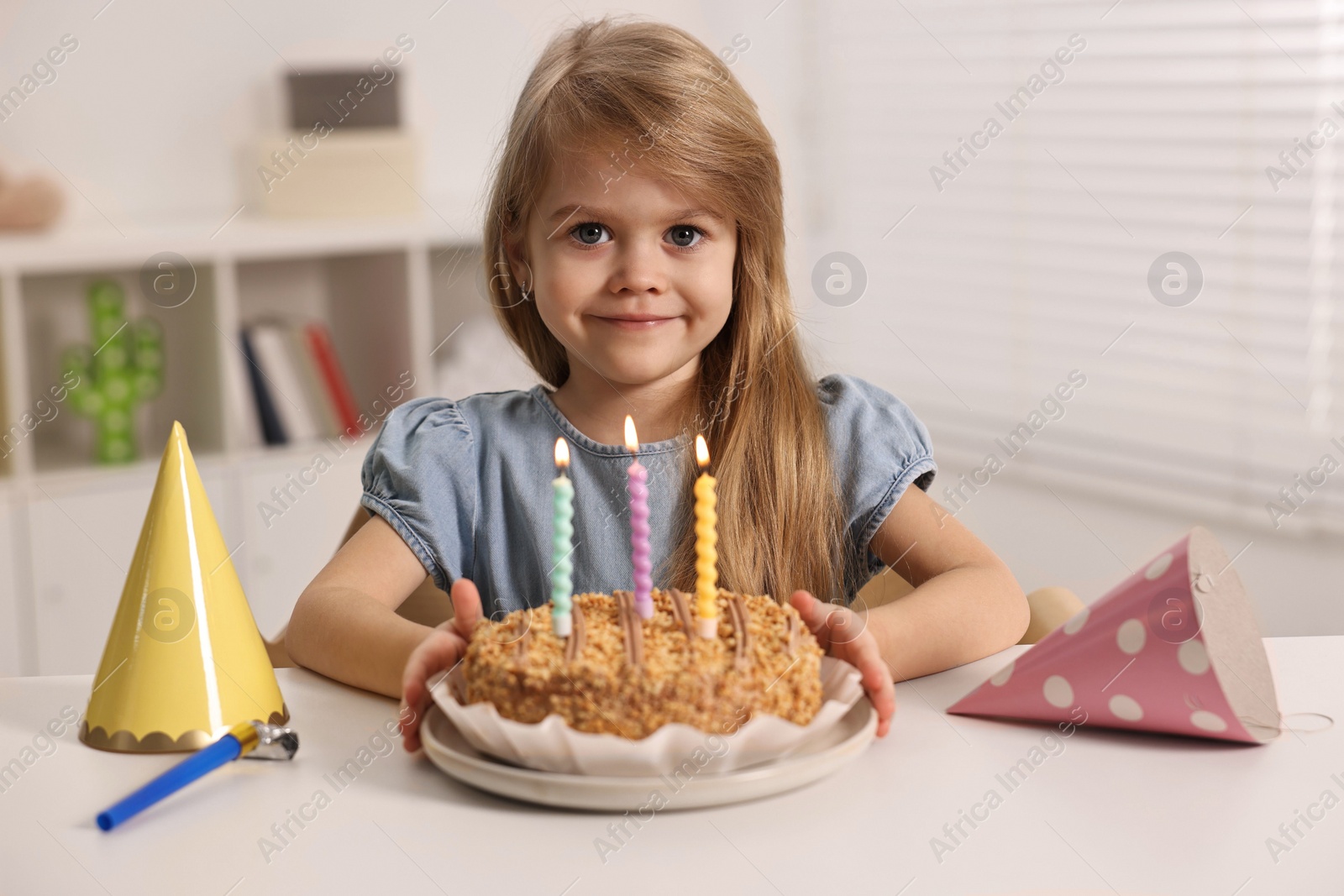 Photo of Cute girl with birthday cake at table indoors