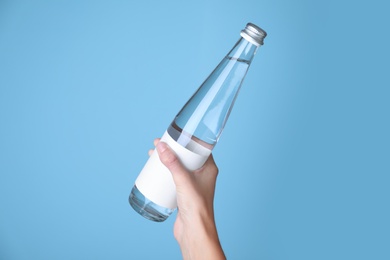 Photo of Woman holding glass bottle with soda water on light blue background, closeup