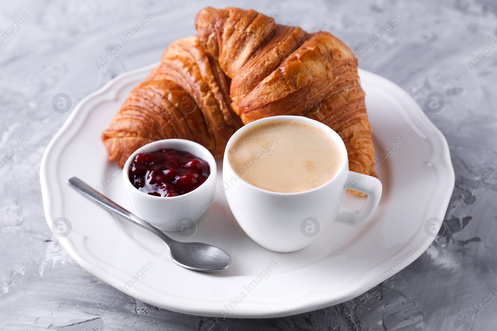 Photo of Tasty breakfast. Cup of coffee, fresh croissants and jam on grey table