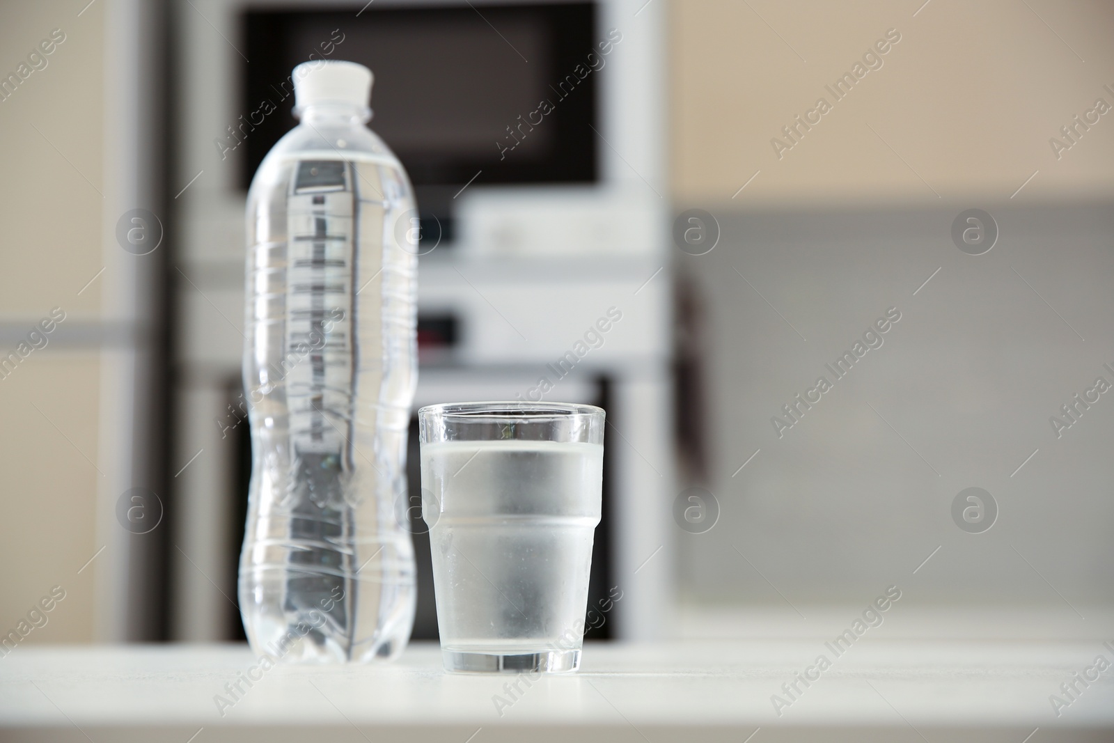 Photo of Glass and plastic bottle with water on table in kitchen. Space for text