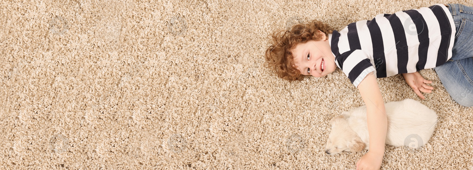 Image of Little boy with cute puppy on beige carpet, top view. Banner design