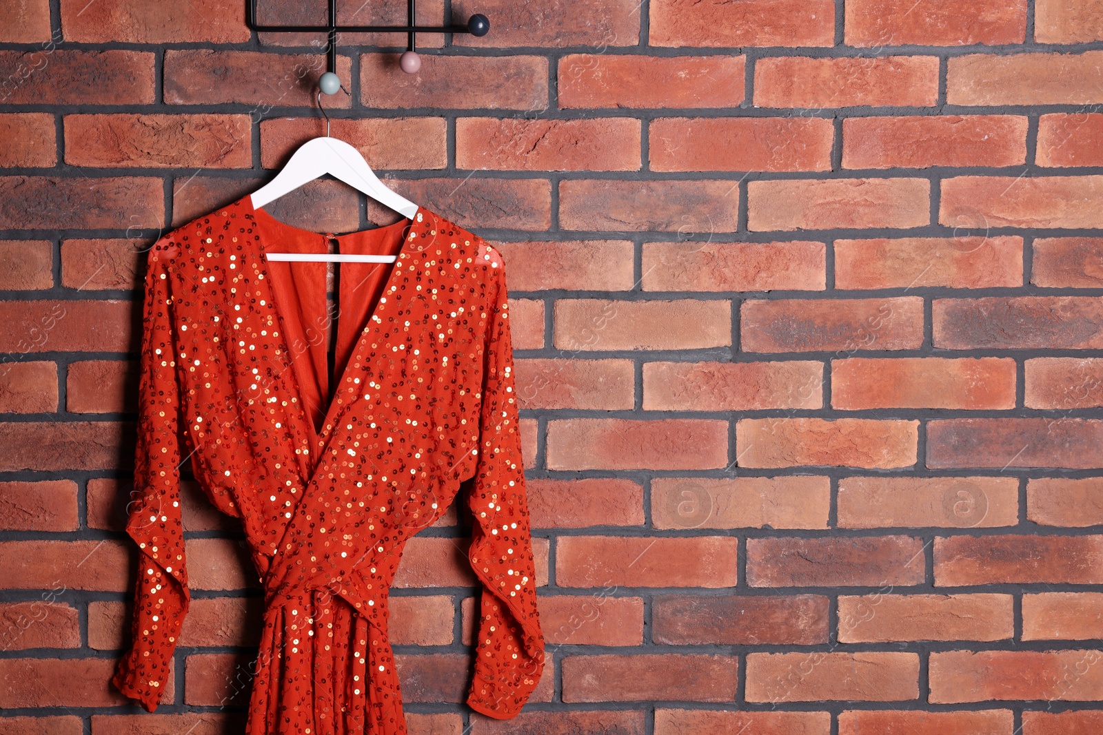 Photo of Beautiful red women's party dress on hanger near brick wall., space for text. Stylish trendy clothes for high school prom