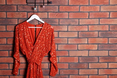 Photo of Beautiful red women's party dress on hanger near brick wall., space for text. Stylish trendy clothes for high school prom