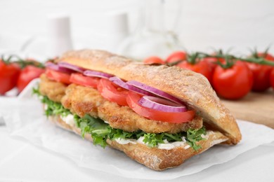 Delicious sandwich with schnitzel on white tiled table, closeup