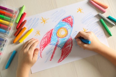 Photo of Little boy drawing rocket with soft pastel at wooden table, top view. Child`s art