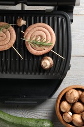 Photo of Electric grill with homemade sausages, rosemary and vegetables on rustic wooden table, flat lay