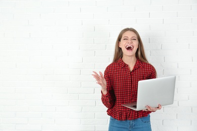 Photo of Emotional young woman with laptop celebrating victory near brick wall. Space for text