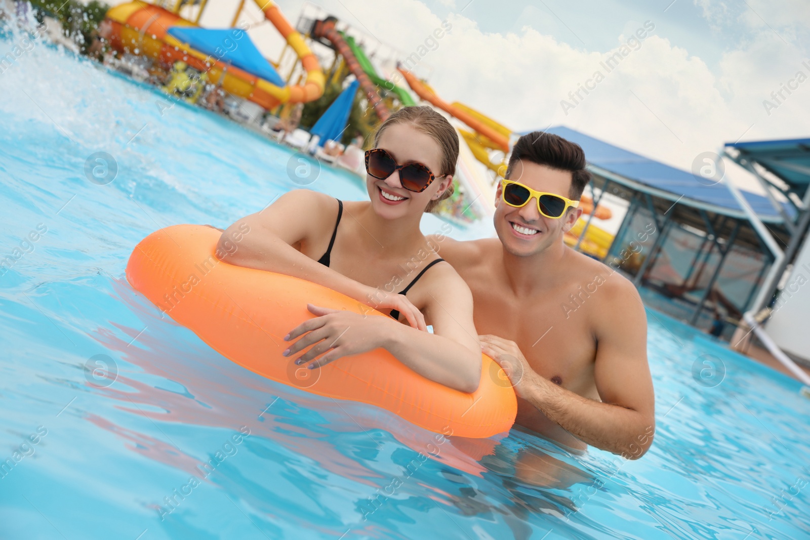 Photo of Happy couple with inflatable ring in swimming pool at water park