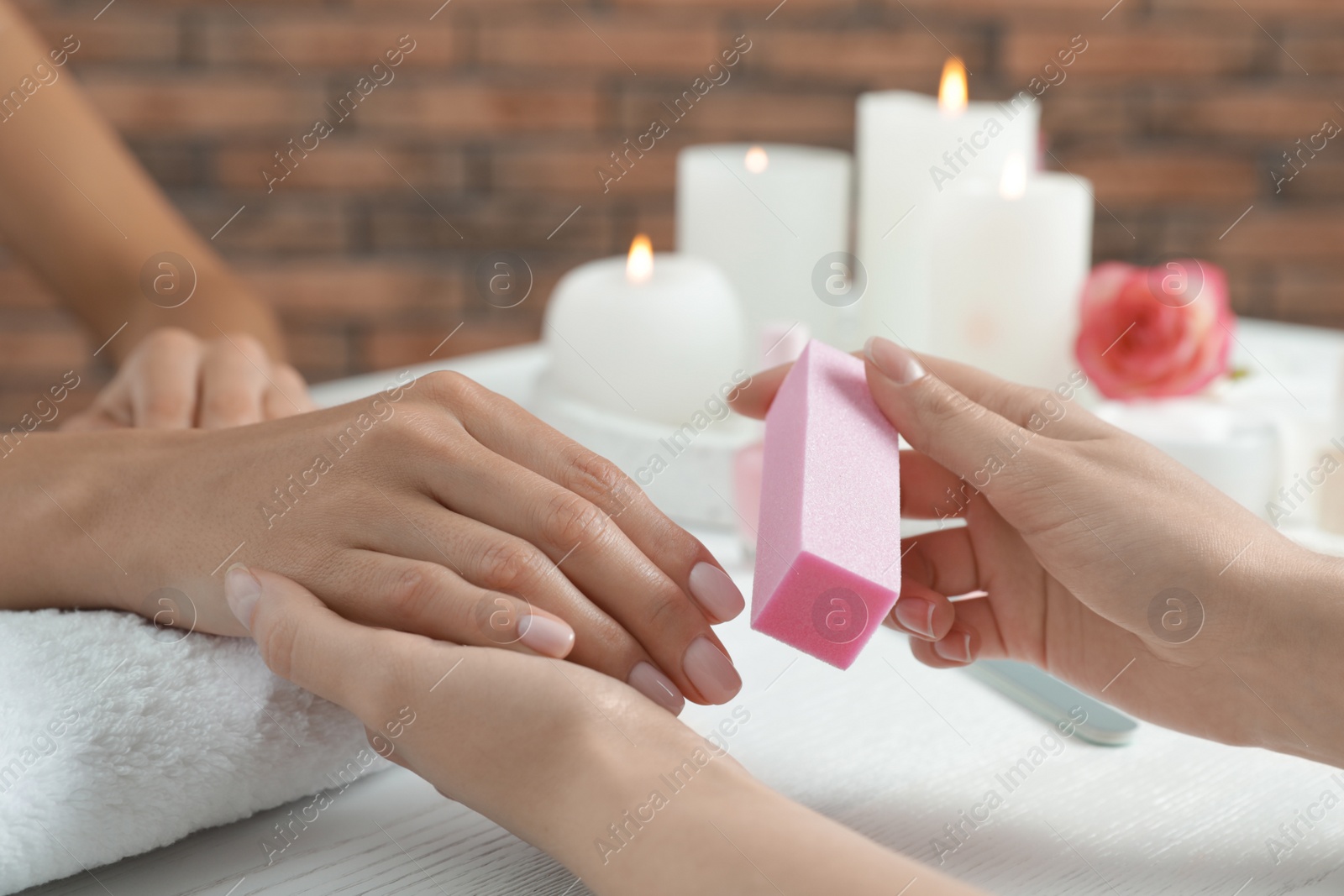 Photo of Manicurist polishing client's nails with buffer at table, closeup. Spa treatment
