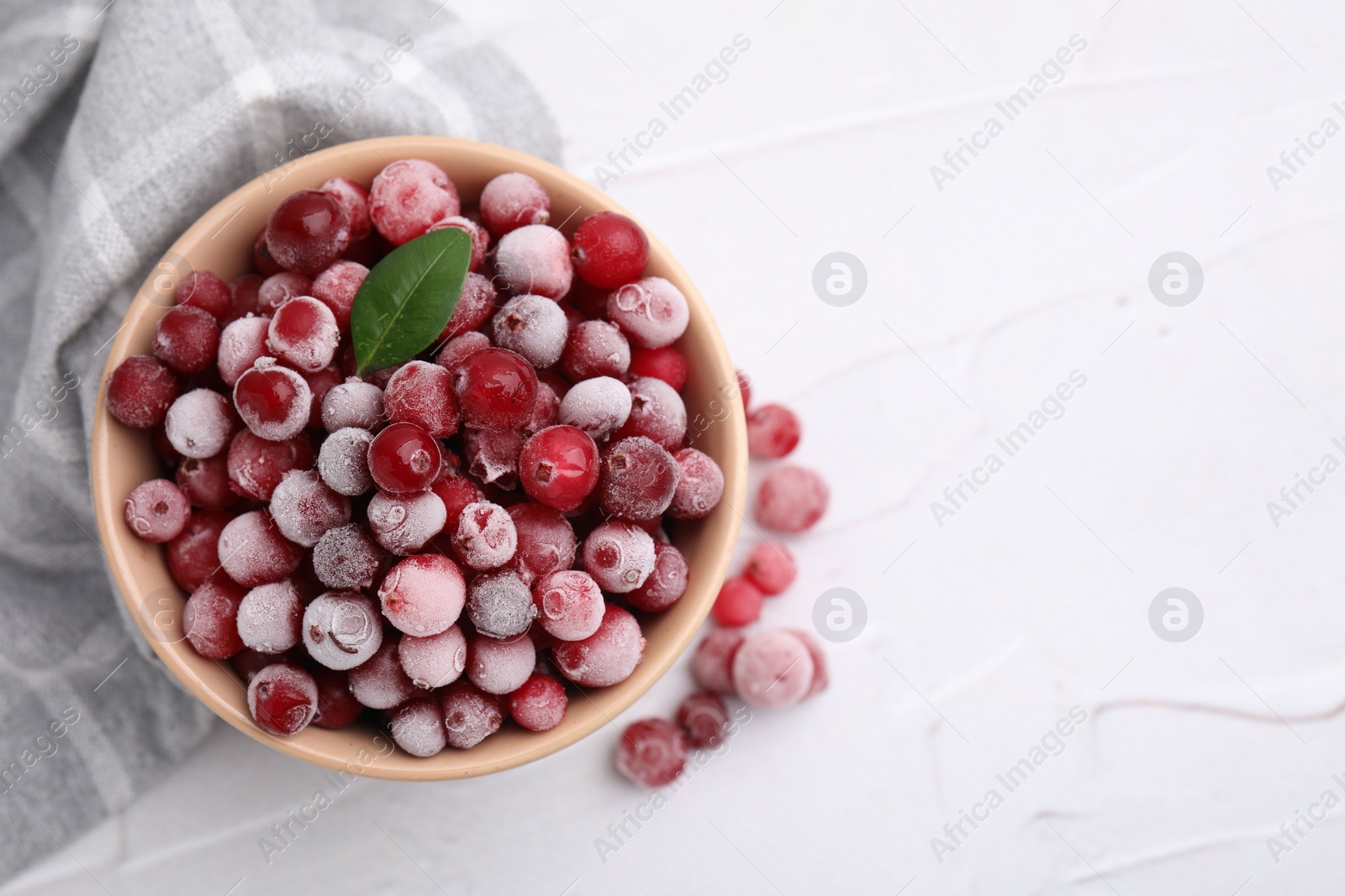 Photo of Frozen red cranberries in bowl on white table, top view. Space for text