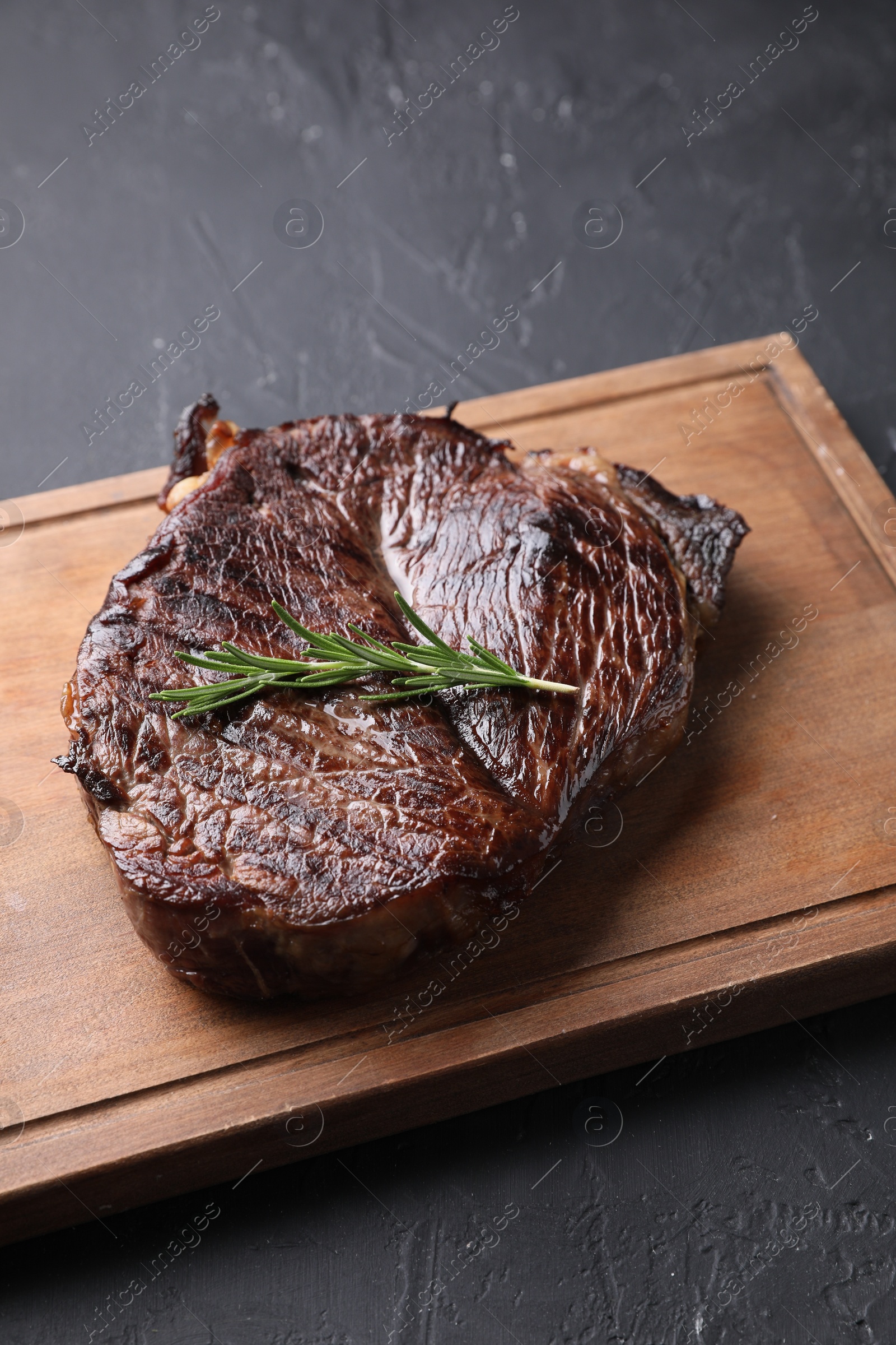 Photo of Wooden board with delicious fried beef meat and rosemary on grey textured table