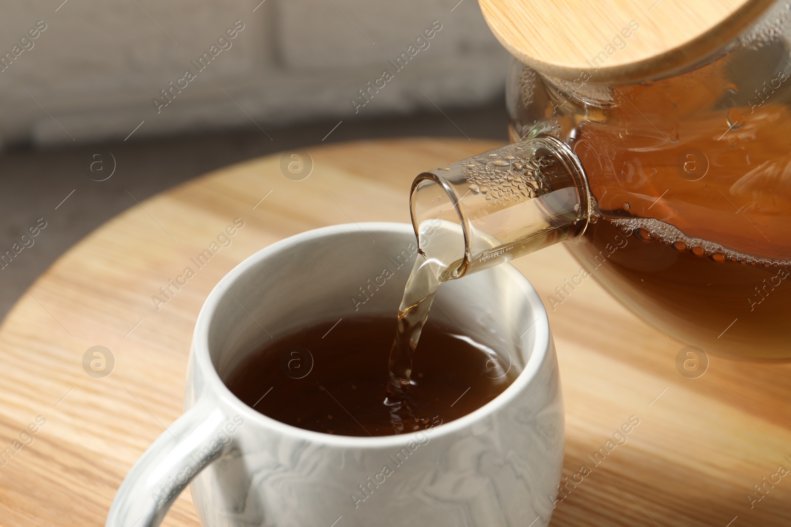 Photo of Pouring aromatic tea in cup at table, closeup