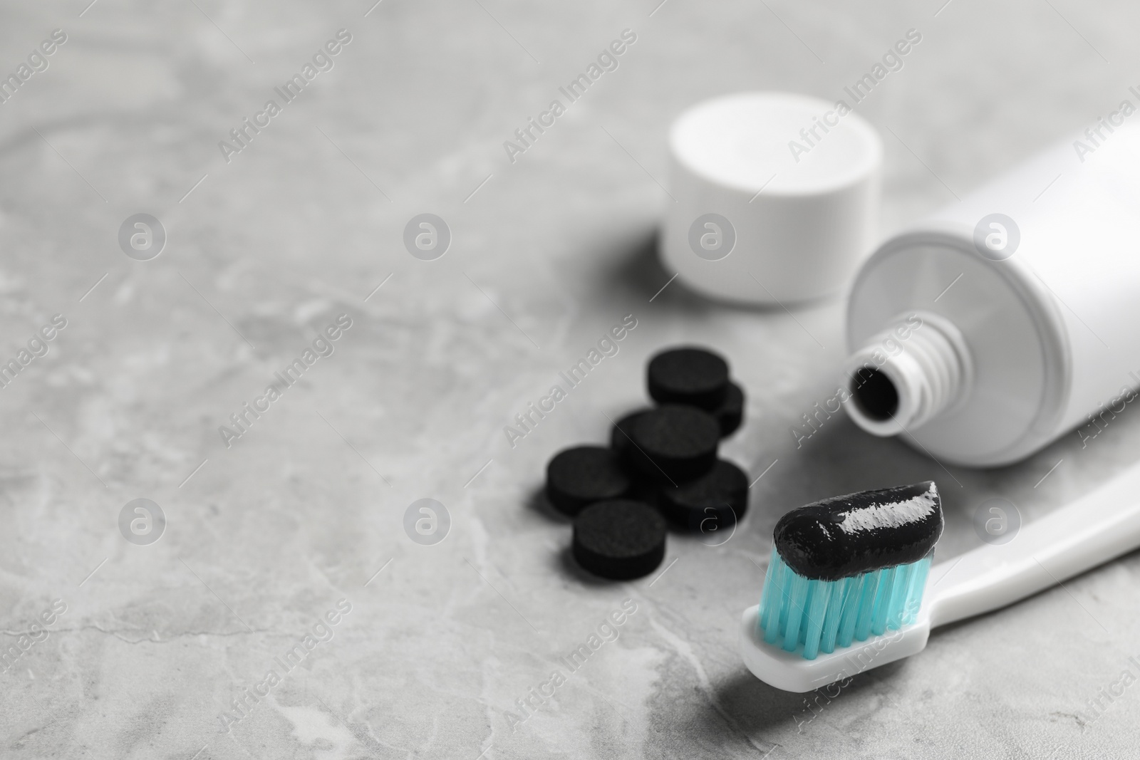 Photo of Brush with charcoal toothpaste on light grey table. Space for text