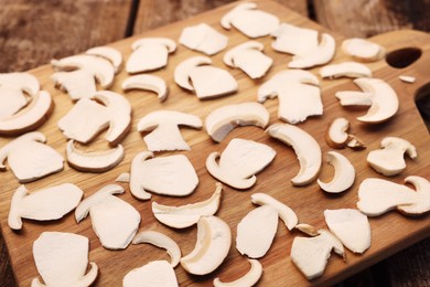 Board with slices of mushrooms on wooden table prepared for natural dehydration, closeup