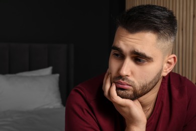 Photo of Sad young man at home. Space for text