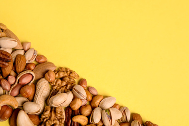 Photo of Different delicious nuts on yellow background, flat lay. Space for text