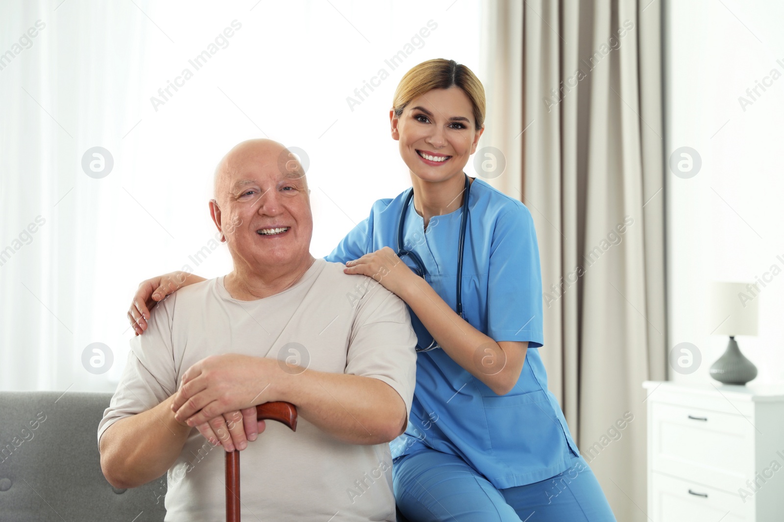 Photo of Nurse assisting elderly man with cane indoors