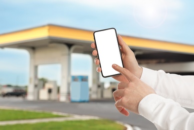 Image of Man paying for refueling via smartphone at gas station, closeup. Device with empty screen