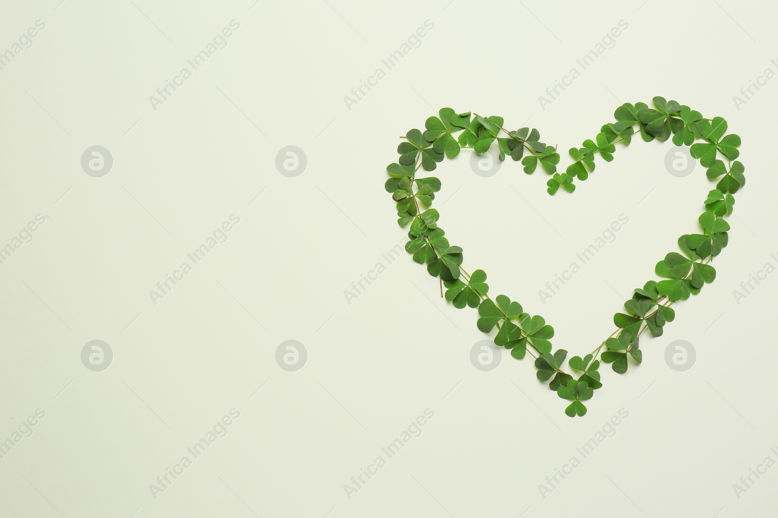Photo of Heart of green clover leaves on light background, flat lay. Space for text