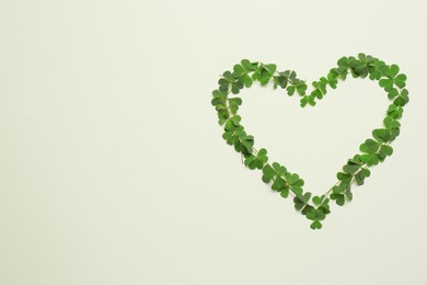 Heart of green clover leaves on light background, flat lay. Space for text