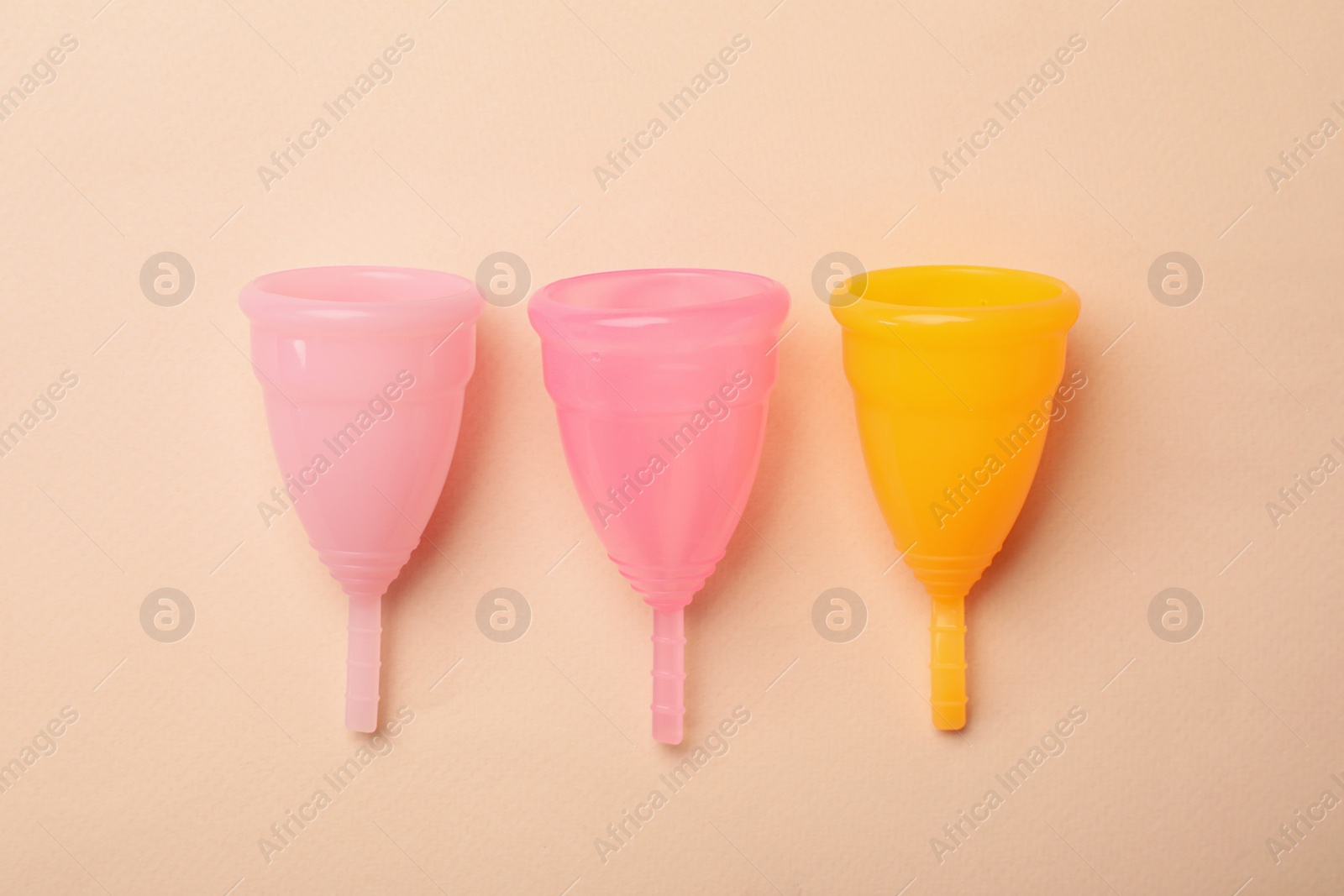 Photo of Menstrual cups on beige background, flat lay