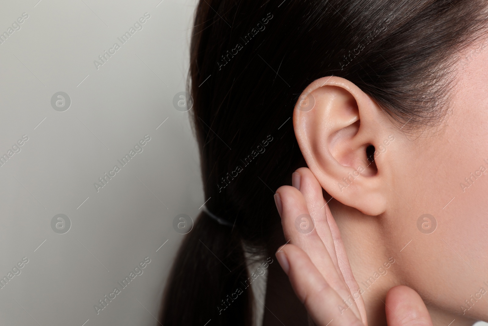 Photo of Woman showing hand to ear gesture on light background, closeup. Space for text
