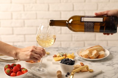 Photo of Woman pouring wine from bottle into glass over table with different snacks, closeup