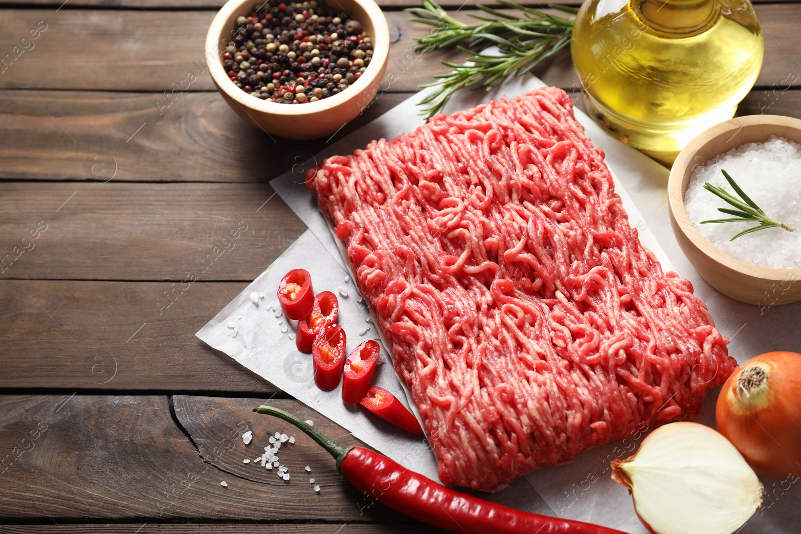 Photo of Raw ground meat, spices, rosemary, oil and onion on wooden table, space for text