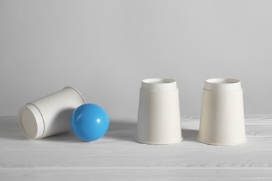 Photo of Shell game. Three paper cups and ball on white wooden table