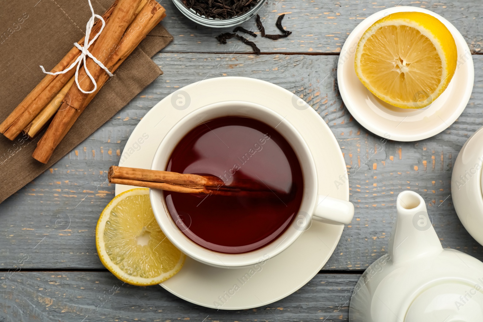 Photo of Delicious hot tea with cinnamon and lemon on grey wooden table, flat lay