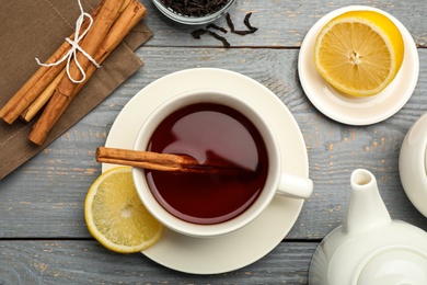 Delicious hot tea with cinnamon and lemon on grey wooden table, flat lay